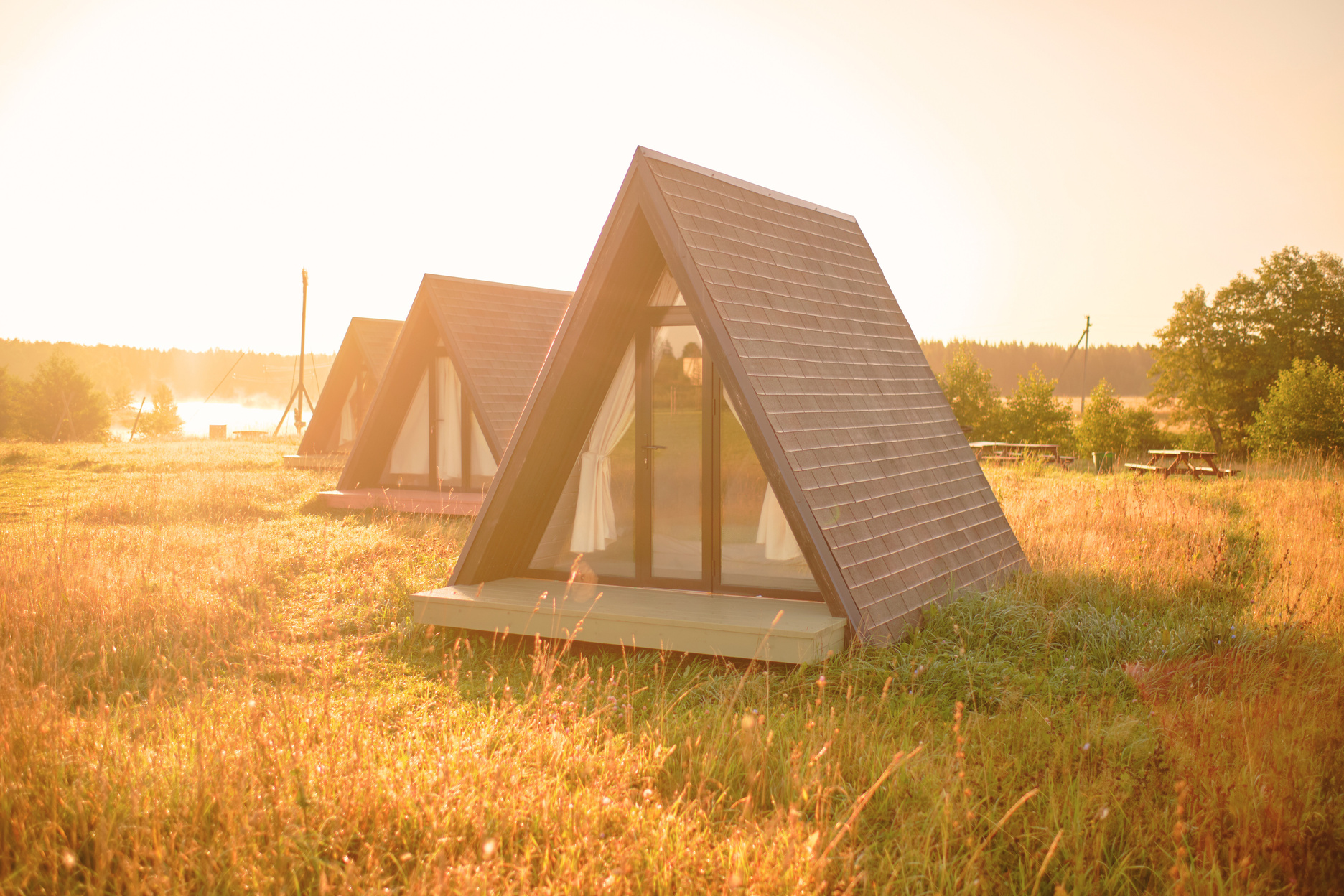 three small cabins in a grassy field with the sun setting behind them